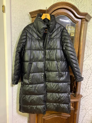 Svart pufferjacka från Cecil Outerwear - Säljer en svart, lång pufferjacka från Cecil Outerwear i storlek XL. Jackan har hög krage, två sidofickor och quiltad design med breda paneler. Säljs då den är för stor för mig!