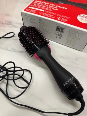 Revlon One-Step Volumiser borste - En svart och rosa elektrisk varmluftsborste från Revlon med oval form och täta borststrån med rosa toppar. Perfekt för att skapa volym och styling i håret med ett enda steg. Ergonomiskt handtag och lång sladd för enkel användning.        Fönborste Revlon ink förpackning, använd endast en gång!!! Kan finnas små hårstrån kvar och vissa ”taggar” kan vara lite böjda av hur den låg i paketet. 800W  Funkar hur bra som helst!!       