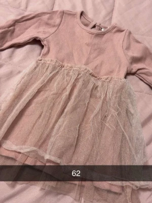 Ljusrosa klänning med tyllkjol fr newbie - Supersöt ljusrosa klänning med ribbad överdel och glittrig tyllkjol. Långärmad modell med rund halsringning och mjukt material.