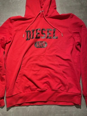Röd hoodie från Diesel med tryck - Snygg röd hoodie från Diesel med stor logga och årtalet 1978 tryckt på bröstet. Klassisk känguruficka framtill, justerbar huva med dragsko och ribbade muddar. Tillverkad i mjukt bomullsmaterial som känns skönt mot huden.