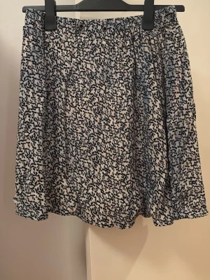 Svartvit kortkjol - Kort kjol i svartvitt blommigt mönster. Kjolen har en luftig passform med lätt volang nertill och resår i midjan. Perfekt för dig som gillar en avslappnad men ändå söt stil.