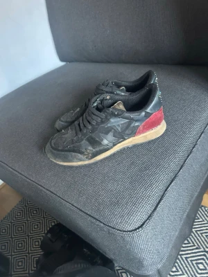 Valentino Rockrunner sneakers svart/röd - Snygga Valentino Rockrunner sneakers i svart mocka och skinn med röda detaljer på hälen. Skorna har klassisk snörning, rund tå och beige sula. Perfekta för dig som vill ha en unik och trendig look med exklusiv känsla.