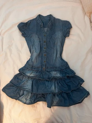Blå jeansklänning med volanger - Säljer denna super snygga & söta klänningen, då den inte kommit till användning. Klänningen har en pytte liten ”defekt” som knappt syns i ryggen. Skriv till mig om ni har frågor!💕