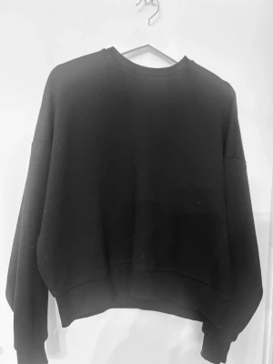 Svart sweatshirt från Nelly - En svart sweatshirt från Nelly i storlek XXS. Tröjan har en klassisk rund halsringning, ribbade muddar och en avslappnad passform. Perfekt för en chill och enkel look. Materialet känns mjukt och bekvämt mot huden.