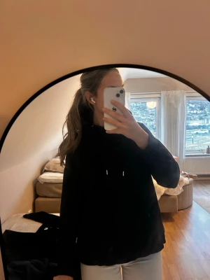 Svart hoodie med huva och magficka - En klassisk svart hoodie med huva och dragsnören. Hoodien har en stor magficka framtill och ribbade muddar vid ärmslut och nederkant. Perfekt för en avslappnad och stilren look. Materialet känns mjukt och bekvämt.