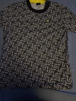 Mönstrad t-shirt från Hugo Boss - Säljer en svartvit t-shirt från Hugo Boss med ett unikt grafiskt mönster över hela plagget. T-shirten har svart krage med gul insida och korta ärmar. Perfekt för dig som vill sticka ut med en stilren men ändå cool look.