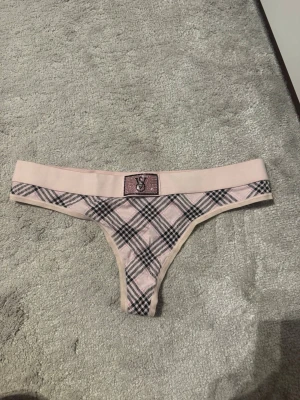 Rosa rutiga stringtrosor VS - Säljer ett par rosa stringtrosor från Victoria's Secret med svart och vitt rutmönster. Trosorna har en bred resår med VS-logga framtill och är tillverkade i ett mjukt och stretchigt material. Perfekta för dig som gillar snygga detaljer och bekväm passform.
