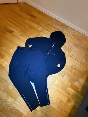Svart träningsset från Under Armour - Säljer ett svart träningsset från Under Armour med matchande hoodie och byxor. Hoodien har dragkedja och logga på bröstet, byxorna har smal passform och diskreta reflexdetaljer. Perfekt för gymmet eller löprundan eller en lugn dag.