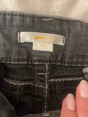 Svarta jeans från Gina Tricot - Snygga svarta jeans från Gina Tricot i storlek 158. Jeansen har klassisk femficksmodell, dragkedja och knappstängning framtill. Materialet är slitstarkt och bekvämt jeans-tyg med tydliga sömmar. Perfekta för en trendig vardagslook.