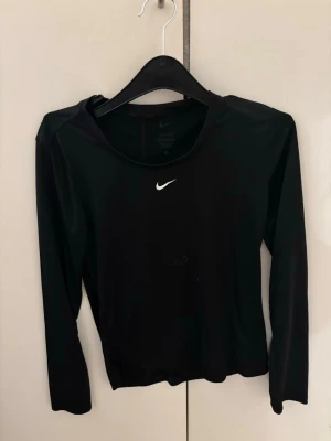 Svart långärmad träningströja Nike - Svart långärmad träningströja från Nike med vit logga på bröstet. Tillverkad i ett stretchigt funktionsmaterial som andas, perfekt för gymmet eller löprundan. Smal passform och rund halsringning ger en sportig look. Har använd den bara 2 gånger.