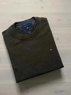 Mörk grön Tommy hilfiger tröja - Mörk grön Tommy Hilfiger-tröja i fint skick. Klassisk och stilren design som passar både till vardag och mer uppklädda tillfällen. Tröjan är väl omhändertagen, utan fläckar eller skador. Postas samma dag vid snabb affär.