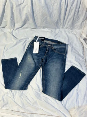 Blå dondup George jeans - Säljer ett par klassiska blå jeans från Dondup med raka ben och snygga slitningar på låret. Jeansen har fem fickor, normal passform och är tillverkade i mjukt bomullsmaterial. Perfekta för en avslappnad och stilren look. Modell george. Helt nya med schyssta slitningar.