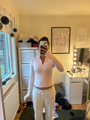 Ljusrosa ziptröja med långa ärmar - Säljer en ljusrosa ziptröja med hög krage och långa ärmar. Tröjan är figurnära och har tumhål vid ärmsluten. Perfekt för lager på lager och enkel att matcha med olika outfits.