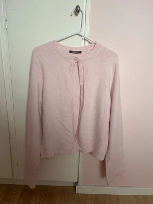 Ljusrosa kofta från Gina Tricot - Söt ljusrosa kofta från Gina Tricot med rund halsringning och knappstängning upptill. Koftan har långa ärmar och är gjord i ett mjukt, stickat material. Perfekt för lager på lager och enkel att matcha med olika outfits.