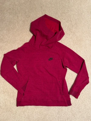 Mörkrosa melerad hoodie från Nike - Snygg mörkrosa hoodie från Nike med svart logga på bröstet. Hoodien har en stor huva, värmande hög krage, långa ärmar och praktiska fickor framtill. Tillverkad i mjukt material som känns skönt mot huden. Junior storlek L(146-156cm) men lite oversized.