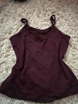 Vinröd linnetopp med spetsdetalj - Snygg vinröd linnetopp med tunna axelband och spetsdetalj vid urringningen. Perfekt att styla till jeans eller kjol för en trendig look. Mjuk och skön känsla, enkel att matcha med olika outfits. Den är från lager 157 I storlek M och passar mig perfekt! Lappen klippte jag av pga att den kliade!