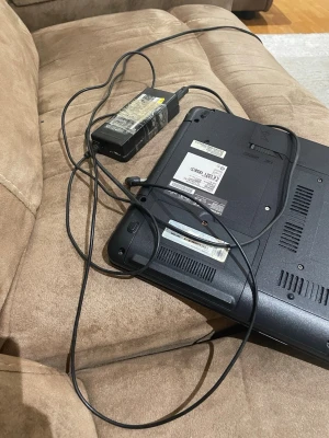 Svart Fujitsu bärbar dator - Säljer en svart bärbar dator från Fujitsu med klassisk design och robust plastchassi. Undersidan har flera ventilationsgaller och etiketter med modellinformation. Laddare medföljer. Perfekt för studier eller vardagsanvändning.