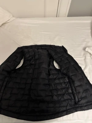 Svart Everest väst - Snygg svart dunväst med quiltat mönster och två fickor framtill. Västen har en klassisk, något längre passform och är perfekt för lager-på-lager. Tillverkad i lätt och smidigt material som håller värmen utan att kännas klumpig.