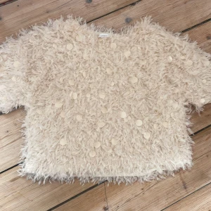 Beige fluffig topp med paljetter Zara - Supercool fluffig topp från Zara i beige med kort ärm. Toppen är täckt av stora, runda paljetter som ger en unik och festlig look. Materialet är syntetiskt och har en lurvig, nästan pälsliknande känsla. Perfekt för dig som vill sticka ut med en statement-piece!