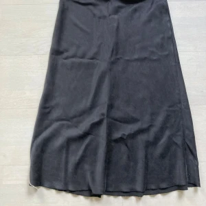 Svart satinkjol från Ahvar Gally - Supersnygg svart långkjol i satin siden 93% från Ahvar Gally. Kjolen har en slät midja och ett elegant, lätt glansigt tyg som ger en lyxig känsla. Perfekt för dig som gillar stilrena och trendiga plagg med en klassisk vibe. Lite grå svart köpt för 2000kr som ny. 