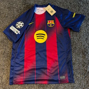 FC Barcelona Lamine Yamal matchtröja Nike M - Säljer en officiell FC Barcelona matchtröja från Nike med Lamine Yamal och nummer 10 på ryggen. Tröjan är blå och röd med gula detaljer, randigt mönster, klubbmärke på bröstet och Champions League-patch på ärmen. Tillverkad i Dri-FIT polyester för bästa komfort.