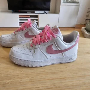 Nike Air Force 1 vit/rosa sneakers - Sälher ett par Nike Air Force 1 '07 Next Nature I storlek 36,5 Använd högst fem gånger då de inte passade i storlek. Finns vita orginal snören till samt att kartongen finns kvar