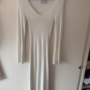Vit ribbad långklänning från Aware - Supersnygg långklänning från Aware i ribbad vit trikå. Klänningen har lång ärm, v-ringning och sitter figurnära över kroppen. Perfekt för dig som gillar stilrena och enkla plagg med en modern touch.