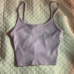 Ljuslila ribbad linnetopp - Säljer en ljuslila croppad linnetopp med smala axelband och ribbad struktur. Toppen är ärmlös och har en enkel, stilren design som passar perfekt till sommaren. Materialet känns mjukt och stretchigt, vilket gör den superbekväm att bära! ❤️
