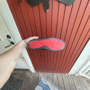 Christian Louboutin svarta sneakers mocka - Svarta sneakers i mocka från Christian Louboutin med ikonisk röd sula och svarta nitar på tån. Skorna har snörning och en platt sula, vilket ger en edgy och lyxig vibe. Perfekta för dig som vill sticka ut med exklusiva detaljer och streetstyle.