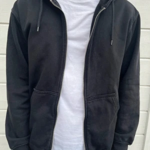 Svart hoodie från Weekday - En svart hoodie från Weekday med dragkedja framtill och huva. Tröjan har långa ärmar och en klassisk, enkel design som passar perfekt till chill dagar. Materialet känns mjukt och bekvämt, och modellen är normal i passformen. Den sitter utmärkt och använd 2 gånger hemma! Pris kan självklart diskuteras !