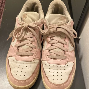 Nike Air Force 1 rosa och vita sneakers - Nike Air Force 1 sneakers i en snygg kombo av ljusrosa och vitt. Klassisk siluett med rund tå, snörning och platt sula. Ovandel i skinn och textil, med ikonisk Nike-logga på sidan. Perfekta för dig som vill ha en stilren och trendig look.