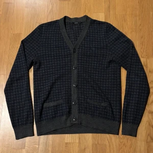 Mörkblå och grå rutig kofta från Adam - Snygg kofta från Adam i mörkblått och grått med klassiskt rutigt mönster. Koftan har v-ringning, knappar framtill och två fickor. Perfekt för lager-på-lager och passar till både jeans och chinos.