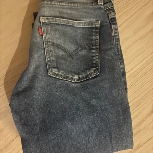 Levi's blå jeans straight fit -  Klassiska blå jeans från Levi's med raka ben och snyggt slitna detaljer. Jeansen har fem fickor, normal passform och ikonisk röd Levi's-tag på bakfickan. Perfekta till sneakers eller boots och tillverkade i robust denim.