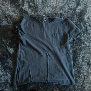 Mörkblå t-shirt från Dobber - Säljer en enkel och stilren mörkblå t-shirt från Dobber med rund hals och en liten bröstficka. T-shirten är kortärmad och gjord i mjuk bomull, perfekt för dig som gillar en clean look. Passformen är normal och funkar till många olika stilar.