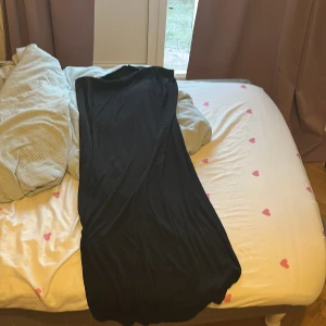 Svart långkjol från 157 - Svart långkjol från 157 i mjukt bomullsmaterial. Kjolen har en enkel och stilren design med rak passform och är ärmlös. Perfekt för dig som gillar minimalistisk stil och vill ha en kjol som är lätt att matcha med accessoarer.