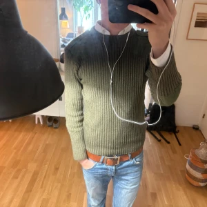 Olivgrön ribbstickad tröja med detaljer - Säljer en olivgrön ribbstickad tröja med förstärkta axel- och armbågspartier i tyg. Tröjan har rund halsringning och långa ärmar, perfekt för lager-på-lager-stil. Snygg och tidlös modell som funkar året runt.