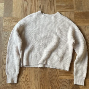 Ljusrosa stickad tröja från Kappahl - Mysig ljusrosa stickad tröja från Kappahl med rund hals och ribbade muddar. Tröjan har en kort passform men är ändå perfekt för lite kyligare dagar. Enkel design utan mönster eller detaljer, passar dig som gillar stilrena plagg.