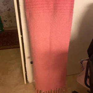 Rosa fluffig halsduk med fransar - En lång, mjuk och fluffig halsduk i en härlig rosa färg. Halsduken har klassiska fransar i ändarna och är perfekt att svepa runt halsen för extra värme. Enkel design utan mönster, passar dig som gillar färg och mysiga accessoarer.