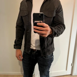 Mörkgrön overshirt från Selected Homme - Snygg grön overshirt från Selected Homme i ekologisk bomull. Jackan har klassisk krage, två bröstfickor med lock och knappar samt långa ärmar. Perfekt lager-på-lager-plagg med stilren look och normal passform. Storlek medium.