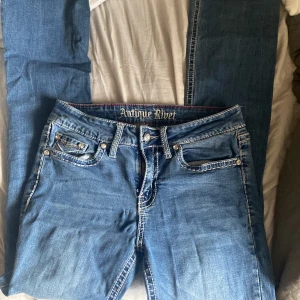 Antique Rivet blå bootcut jeans med broderad ficka - Blå bootcut jeans från Antique Rivet med snygga kontrastsömmar och en unik broderad bakficka med korsmönster. Klassisk femficksmodell och detaljerade nitar. Jeansen är tillverkade i bomull med en liten del spandex för stretch. Jeansen är lagade en gång vid fickan❤️