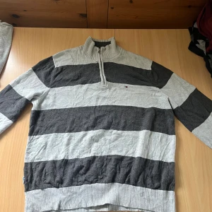 Randig half zip tröja Tommy Hilfiger XL/L - Snygg randig tröja från Tommy Hilfiger i grått och mörkgrått. Tröjan har en ribbad krage med half zip-dragkedja och långa ärmar. Perfekt för dig som gillar klassisk stil med en sportig touch. Tillverkad i mjuk bomull för skön känsla. Änvänd ungefär 1-2 gånger och skickas inom 24 timmar efter du köper. Pris är inte fast kom bara med förslag