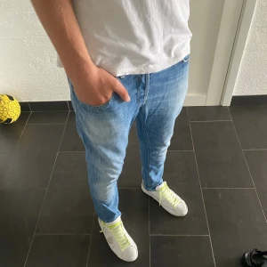 Dondup George - Säljer ett par ljusblå jeans från dondup i storlek 34. Jeansen har en relaxed passform med klassiska fem fickor och snygga slitningar. De är tillverkade i mjukt denimtyg och har orangea sömmar som ger en schysst kontrast. Perfekta för en chill och avslappnad stil.