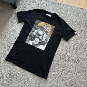 Svart t-shirt med hundtryck från Replay - Svart t-shirt från Replay med ett stort tryck av en hund med gul mössa och text på bröstet. Klassisk passform och rund hals. Perfekt för dig som gillar coola och unika motiv. Skön och mjuk känsla. Storlek M/S