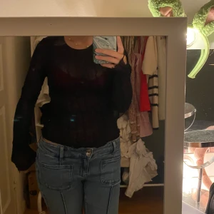 Svart mesh långärmad topp - Säljer en svart, transparent mesh topp med lång ärm. Sitter tight och har ett diskret mönster i tyget som ger en cool look. Perfekt att styla med jeans eller kjol för en trendig outfit. Ett hål vid