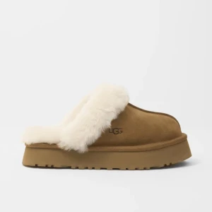 UGG slip-in mockasiner med fårull - Mysiga slip-in skor från UGG i brun mocka med fluffig vit fårullskant. Skorna har en platt sula och är perfekta för kalla dagar när du vill ha det extra bekvämt och varmt om fötterna. Pris går såklart att diskutera och kom privat för bild!