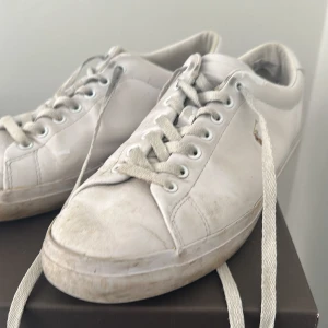 Vita sneakers från Polo Ralph Lauren - Klassiska vita sneakers från Polo Ralph Lauren med snörning och rund tå. Skorna har en stilren design i skinn med den ikoniska polospelaren broderad på sidan. Perfekta för en clean och tidlös look.