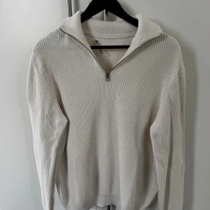 Beige stickad half zip tröja från Zara - Säljer en beige stickad tröja från Zara i storlek L. Tröjan har en snygg krage och half zip-dragkedja framtill. Ribbad struktur och långärmad modell som ger en chill och clean look. Perfekt för lager-på-lager under hösten och vintern.