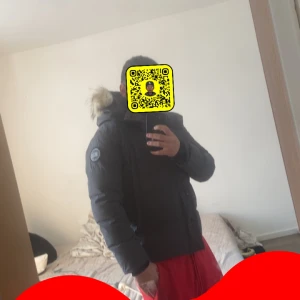 Svart dunjacka Canada Goose med päls - Svart dunjacka från Canada Goose med fet huva och pälsdetalj. Jackan har klassisk patch på ärmen, dragkedja framtill och quiltad design. Perfekt för kalla dagar, riktigt varm och snygg. Passar dig som vill ha en ikonisk vinterjacka med lite mer stil prisvärd jacka. Storlek S men passar M