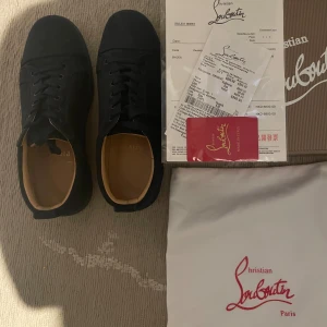 Christian Louboutin svarta sneakers - Mörk blåa sneakers från Christian Louboutin i mocka med klassisk röd sula och rund tå. Skorna har snörning och diskreta detaljer, levereras med originalkartong, dustbag och äkthetskort. Perfekta för dig som vill ha en lyxig och stilren look.