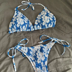 Blåvit blommig bikini - Superfin triangelbikini i blått och vitt med blommigt mönster. Knyts i nacken och ryggen, medan trosan har höga ben och knyt i sidorna. Materialet är smockat och stretchigt för en bekväm passform. Endast testad och därav gott skick. Säljs då den inte passade mig storleksmässigt, lite stor i storleken😊